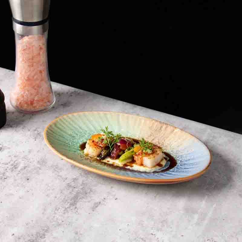 Durable oval porcelain plate styled with gourmet cuisine on a hotel dinner table by a certified ceramic plate supplier